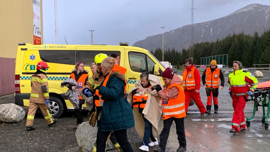 Rescue teams in orange vests walk with passengers wrapped in a blankets