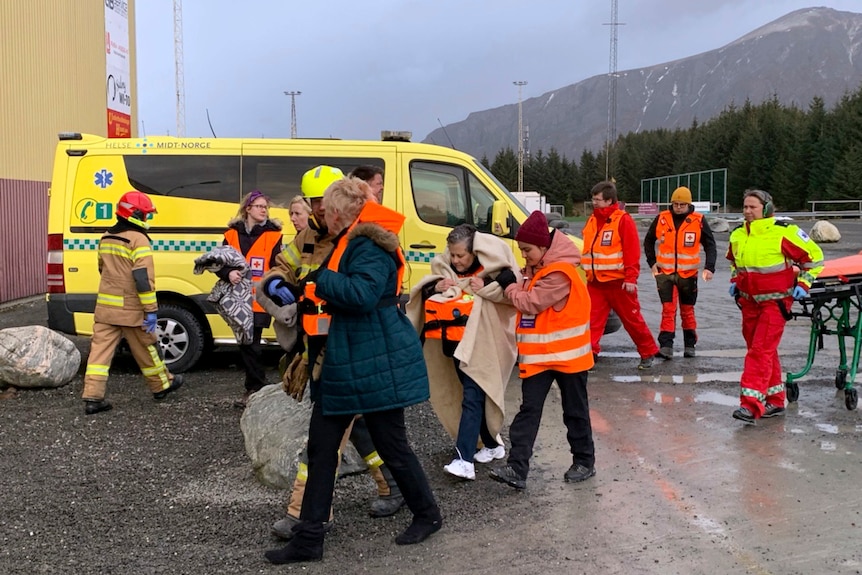 Rescue teams in orange vests walk with passengers wrapped in a blankets