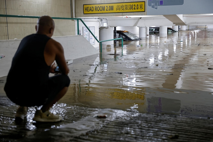 一名男子蹲在车库尽头，看着眼前淹没车库的洪水