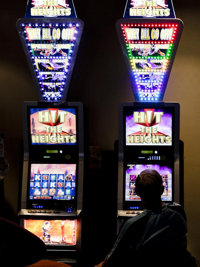 A man plays the pokies in a darkly lit room.