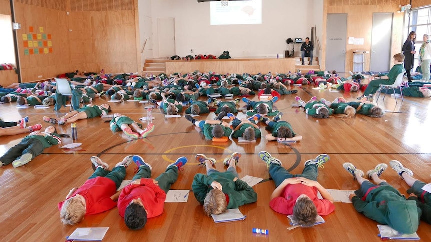 School students lie on the ground in a hall.