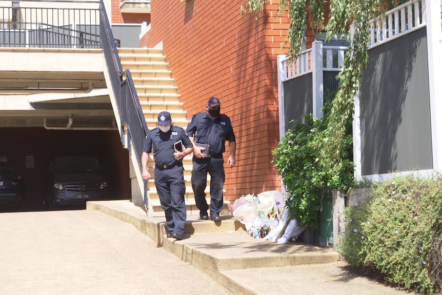 Two police officers walk past floral tributes left on the ground near a block of town houses.