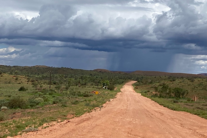 column of dark rain clouds in distance. ochre dirt road.