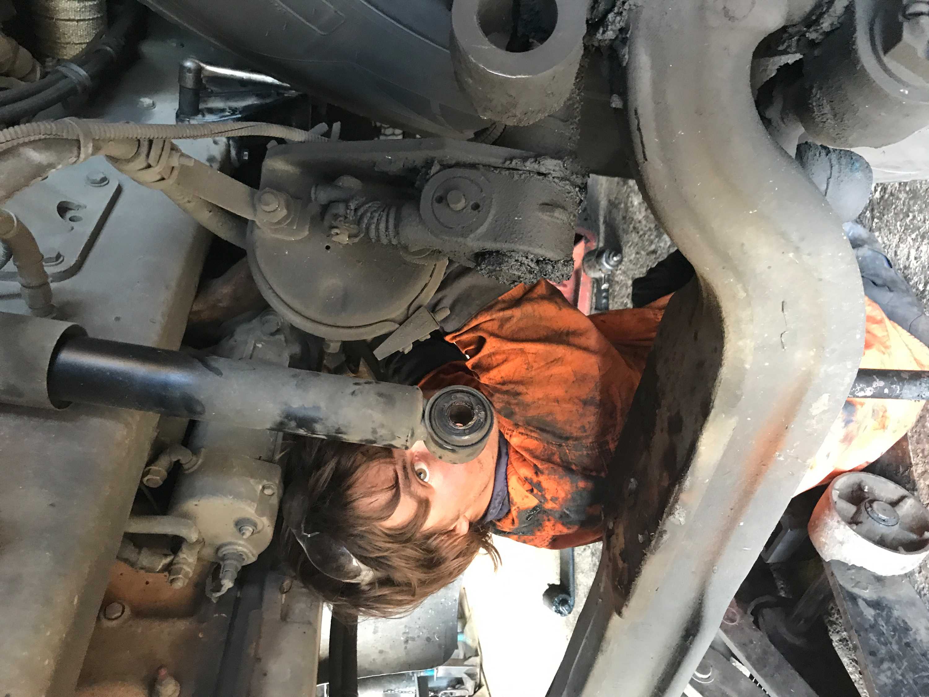 A young man in work clothes under engine of a semi trailer.