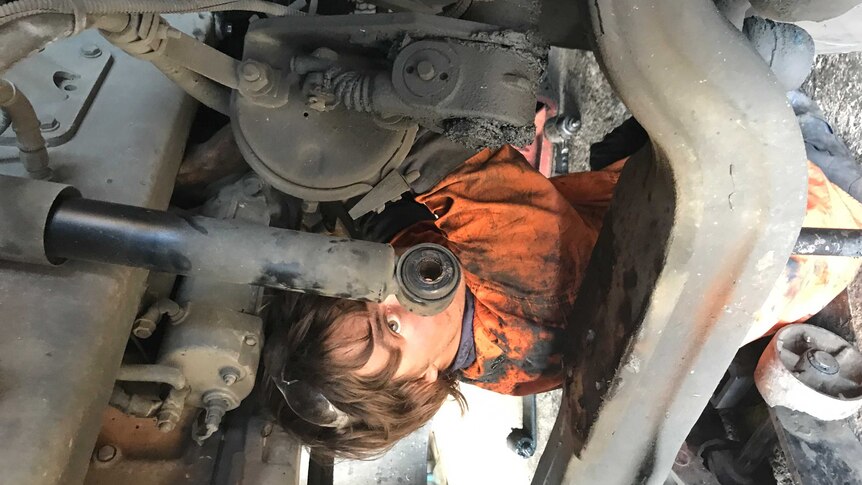A young man in work clothes under engine of a semi trailer.