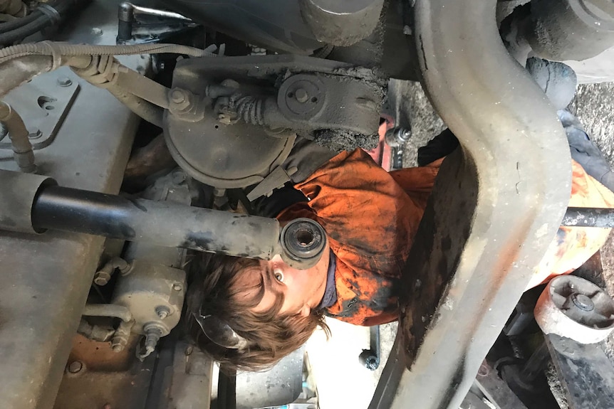 A young man in work clothes under engine of a semi trailer.