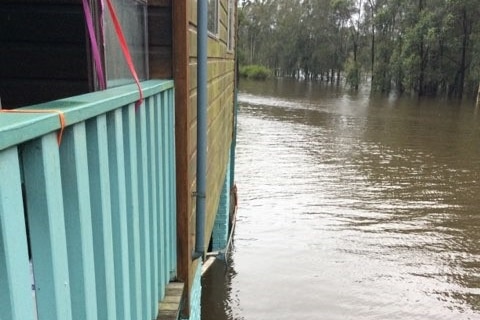 A cream and sky blue weatherboard is submerged in floodwaters.