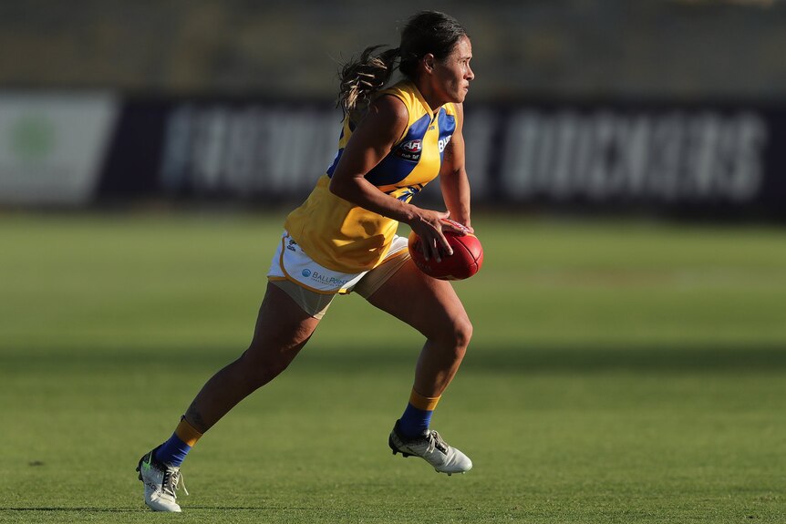 A young indigenous woman playing in the AFLW wearing a yellow guernsey