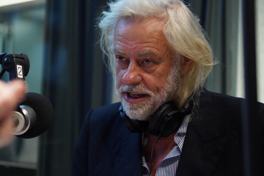 Bob Geldof, a man with long white hair and facial hair looking off camera, speaking into a microphone.