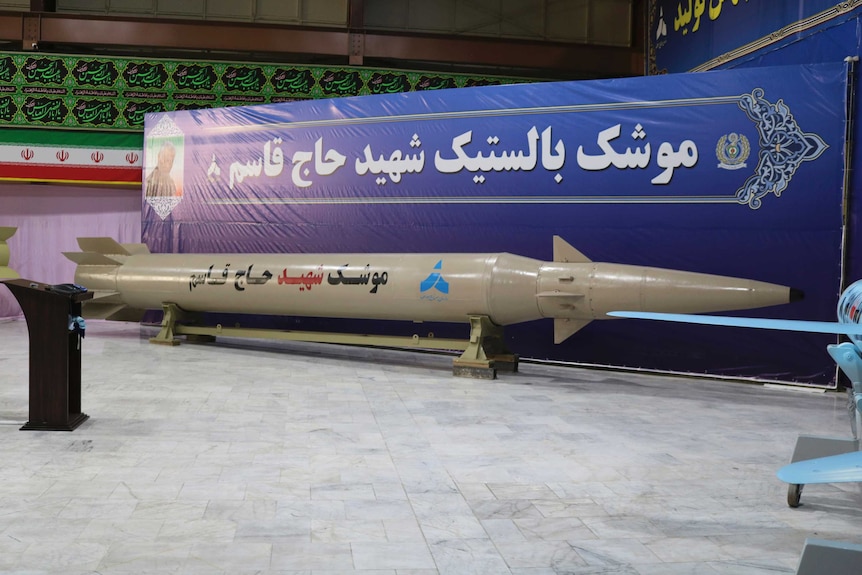 A white missile is displayed in front of a blue banner with Qassem Soleimani's photograph.