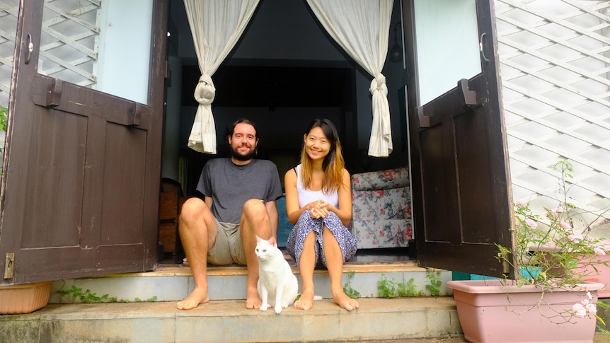 A man and a woman sitting on a front deck with a white cat in front of them