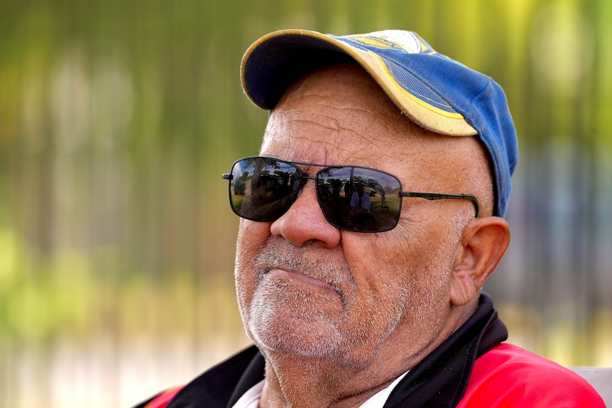 An Aboriginal man with a blue and yellow parramatta eels hat, wearing black sunglasses and a red collared shirt.