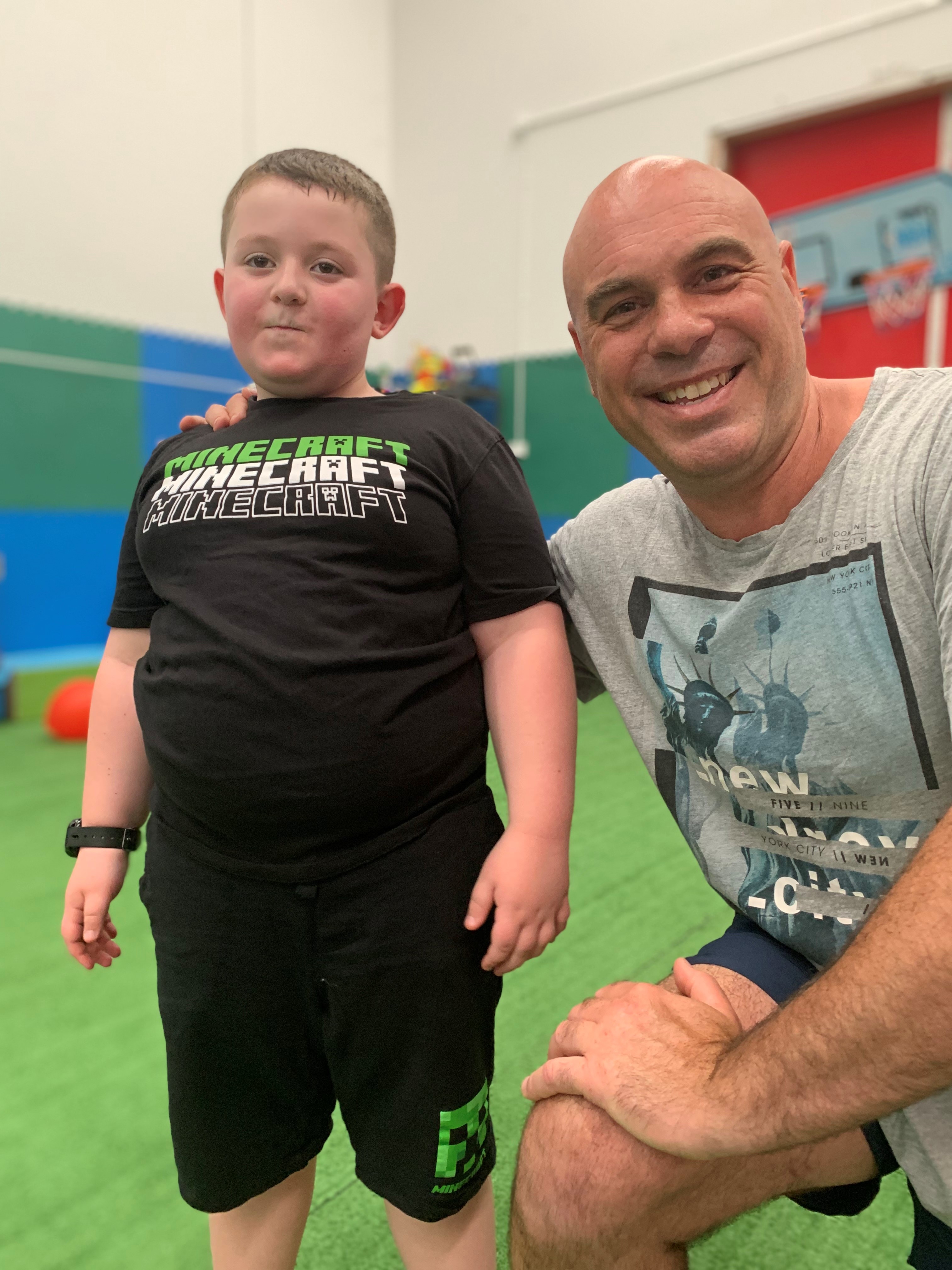 Max Drew stands on an indoor sports court with his sports therapist Jason Nanos kneeling beside him