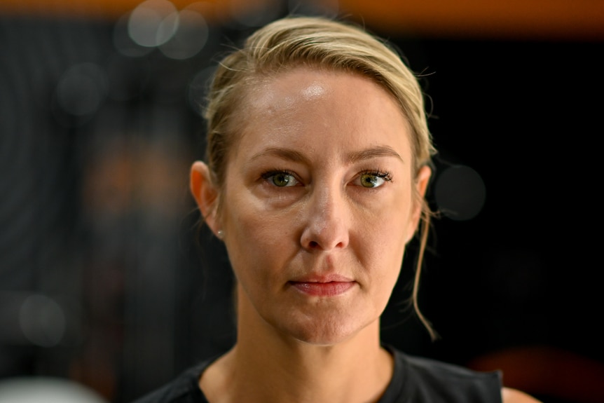 Woman with blonde hair looking to camera with black background