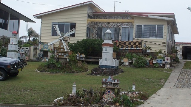 A weatherboard house that has been tiled and ceramic windmills stand tall in the front garden of house.