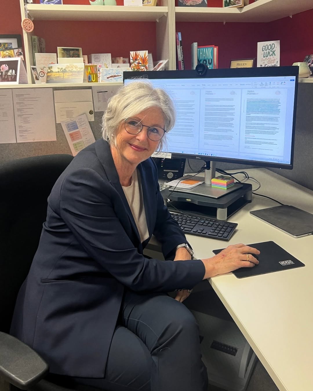 Helen Haines, wearing a blue suit and white blouse, sits at a computer in her office