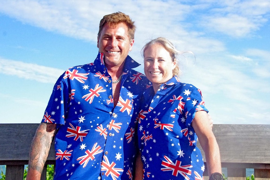 A man and a woman wearing matching Australian flag shirts smile and hug