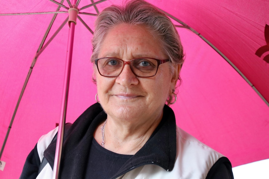 An older woman standing under a pink umbrella