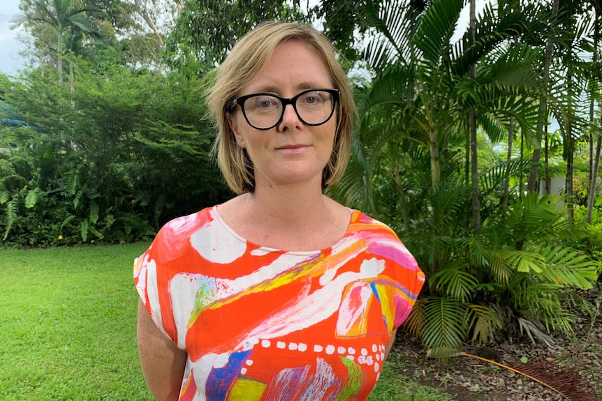 Kirsty Howey is wearing a bright, patterned shirt and has dark glasses on. She is outside in a leafy tropical garden.