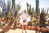 A woman stands with her back to camera holding up arms in front of cactuses.