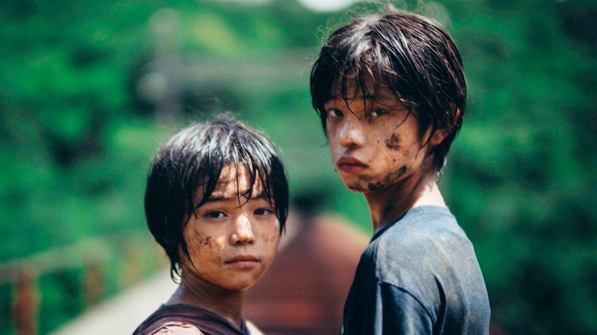 Two children with muddy, sad faces look over their shoulders towards camera