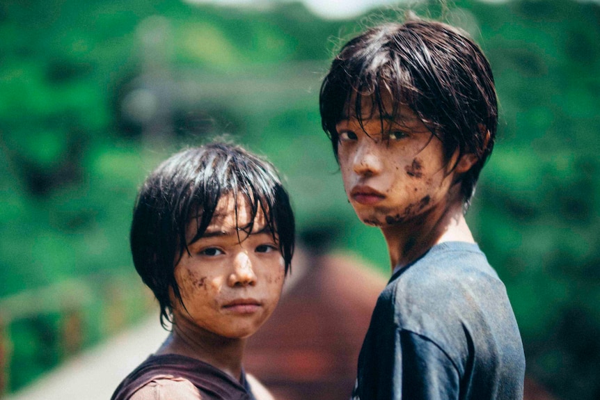 Two children with muddy, sad faces look over their shoulders towards camera