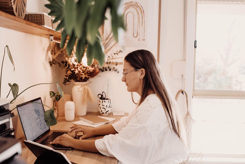A woman work at her computer, in a well decorated room with a plant in the foreground