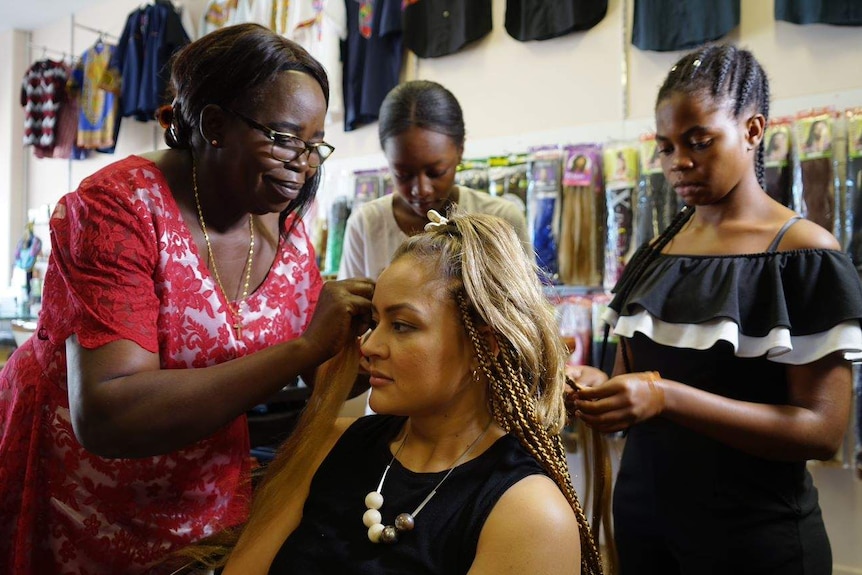 Jean Kute braids a woman's hair at a hair salon.