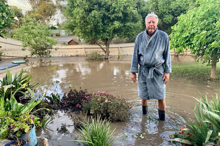 A man in a gray dressing gown stands in his flood backyard