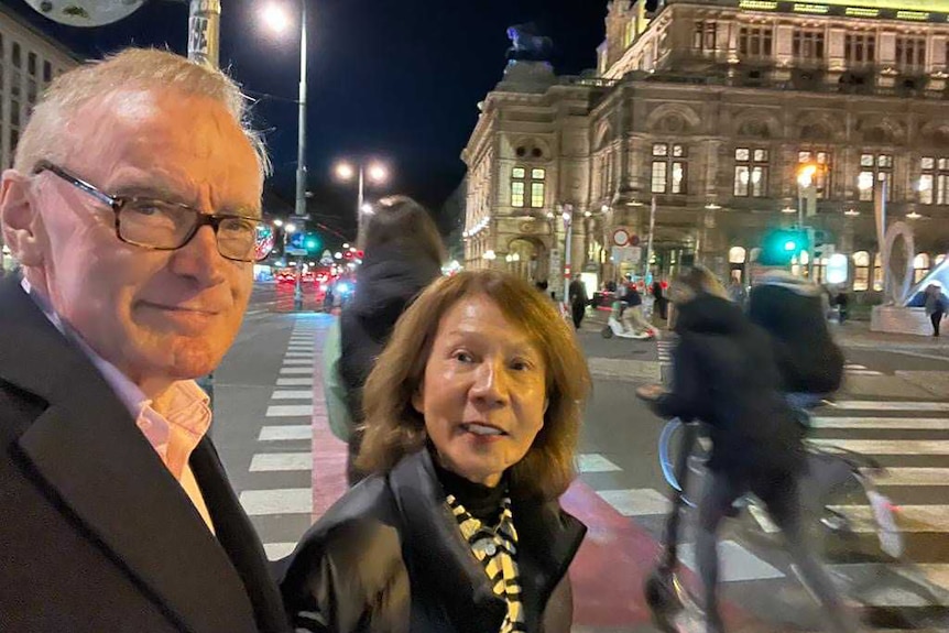 Bob Carr and Helena Carr look toward the camera while walking on a street at night