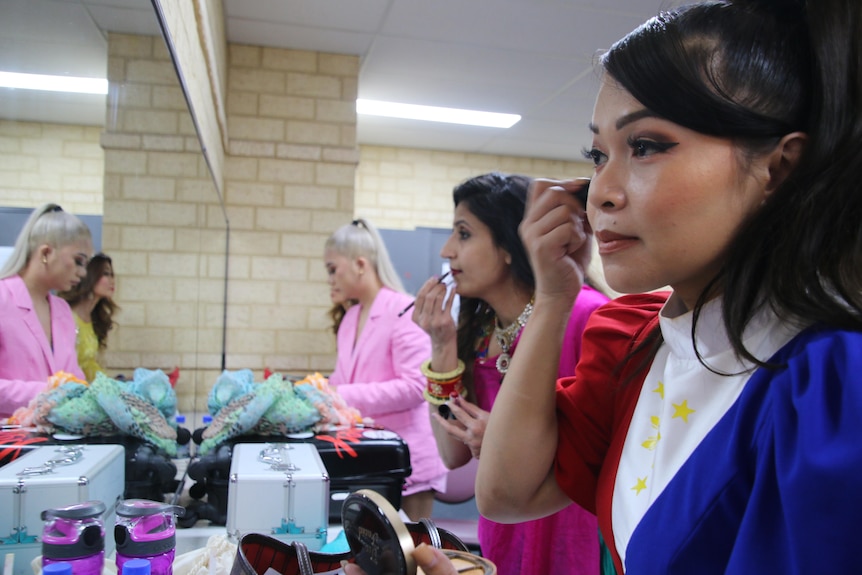 Three migrant models applying make-up backstage