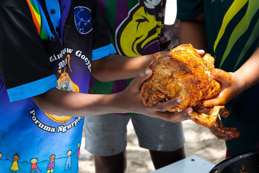 Close up photo of boys holding raw chicken.