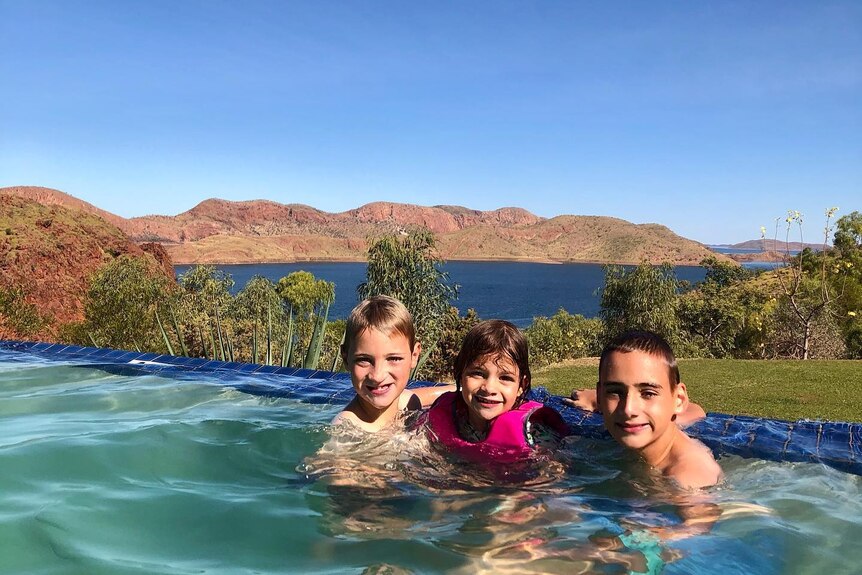 Three kids in a pool with a lake in the background. 