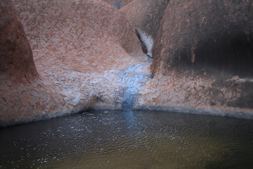 A stream flows into a waterhole surrounded by red rock