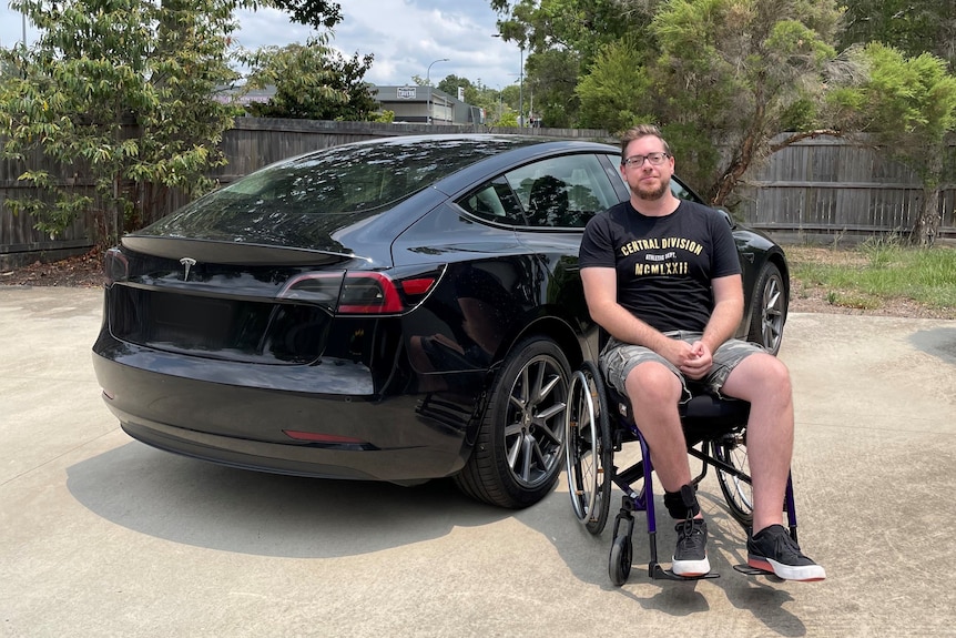 An image of Chris Noble sitting in a wheel chair in front of his electric vehicle 