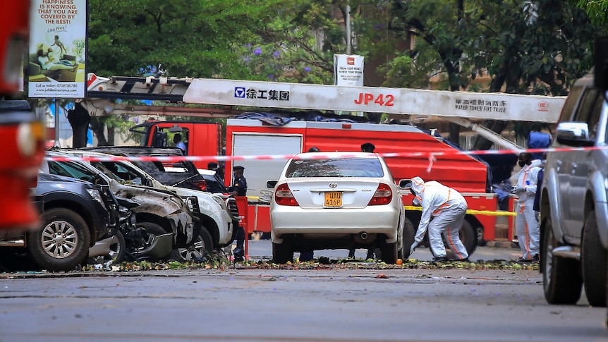 An official examines a car surrounded by police tape and rubble. 