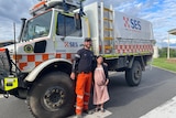 An emergency worker stands in front of a rescue truck with his arm around a pregnant woman.