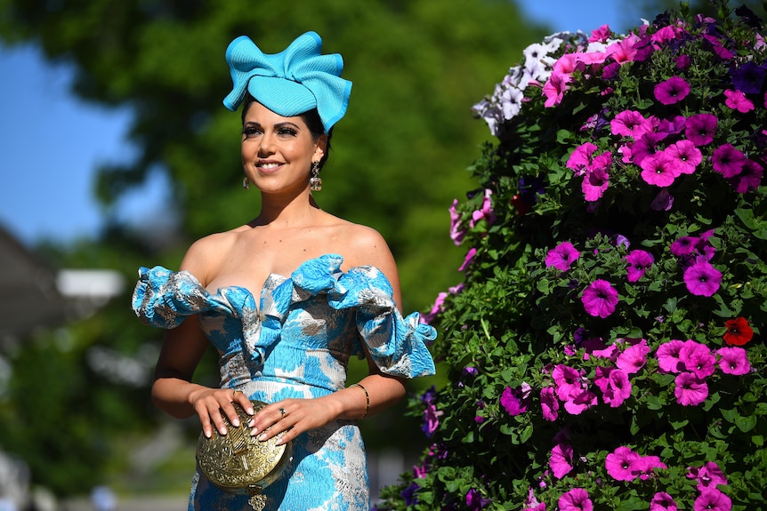A woman wearing a blue outfit next to a bush with bright purple flowers.