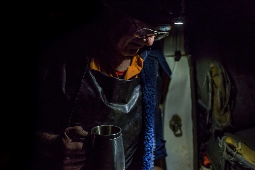 Wearing a warm jacket over his butchering apron, Glenn Cole leans against the door frame of his car, mug in hand and head bowed.