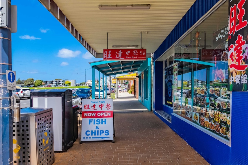 Small town footpath outside a Fish and Chip and Chinese restaurant with cars parked out the front