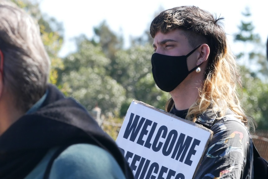 A masked refugee advocate holds a sign "welcome refugees" 