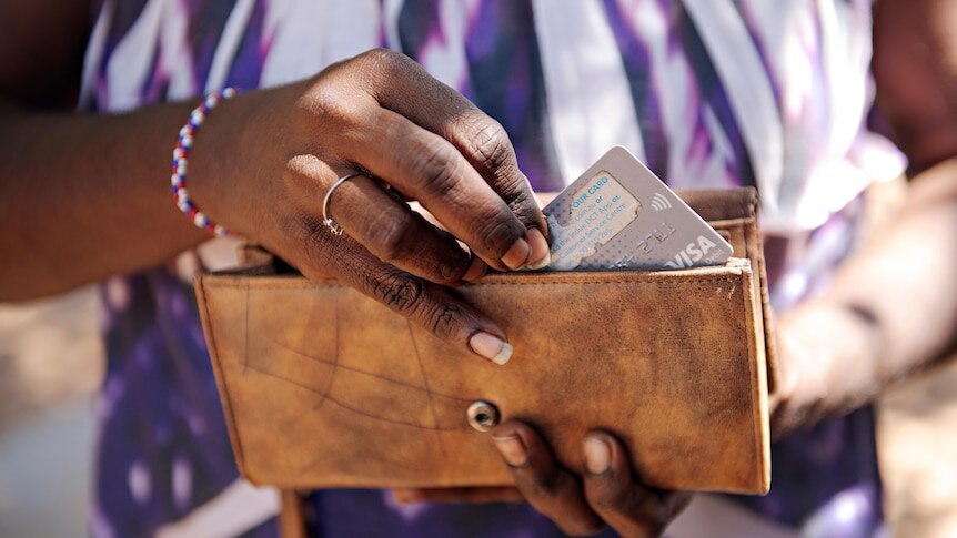 A woman reaches for a debit card from her brown wallet.