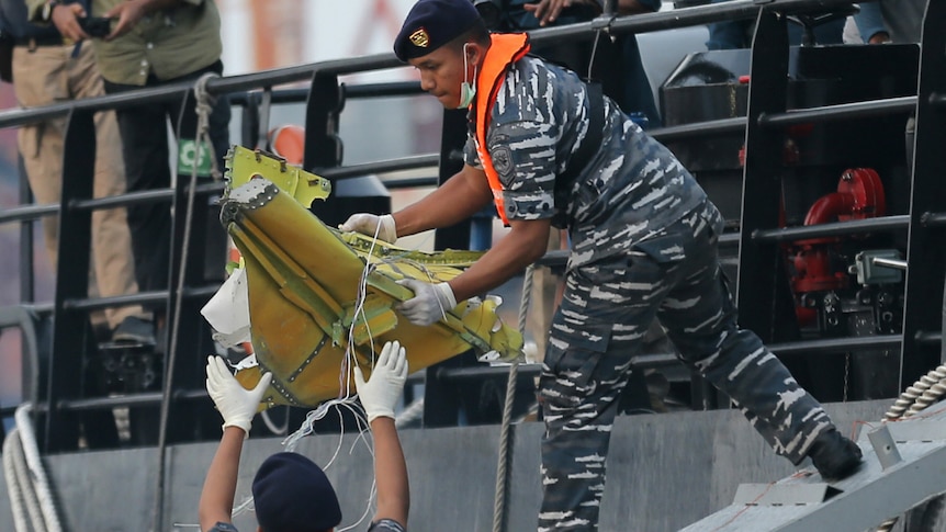 Navy personnel carry a recovered part of the Lion Air jet onto a ship.