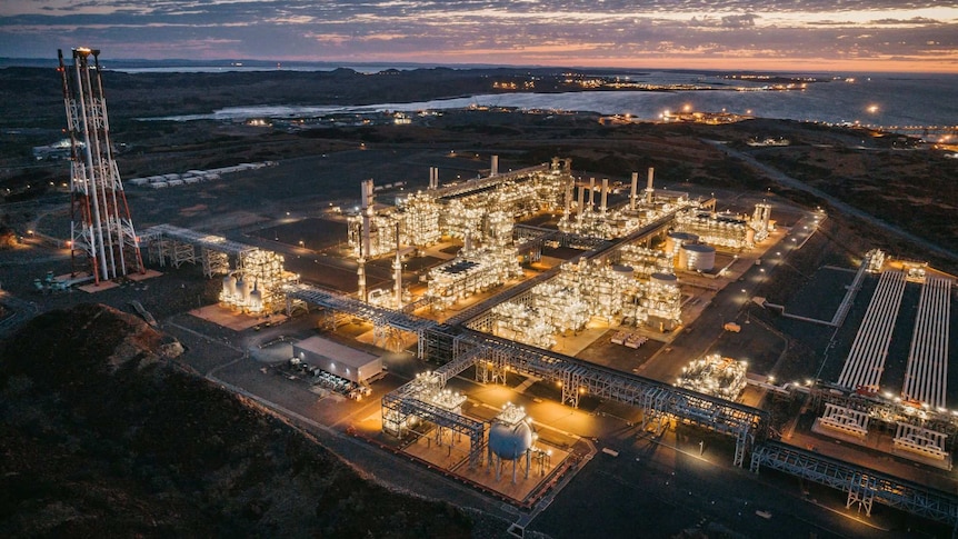 Woodside's Pluto LNG project in the Pilbara lit up with lights at dusk.