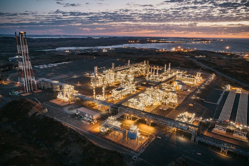 Woodside's Pluto LNG project in the Pilbara lit up with lights at dusk.