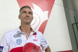 Brett Kirk holds a football while standing in front of a Sydney Swans logo.