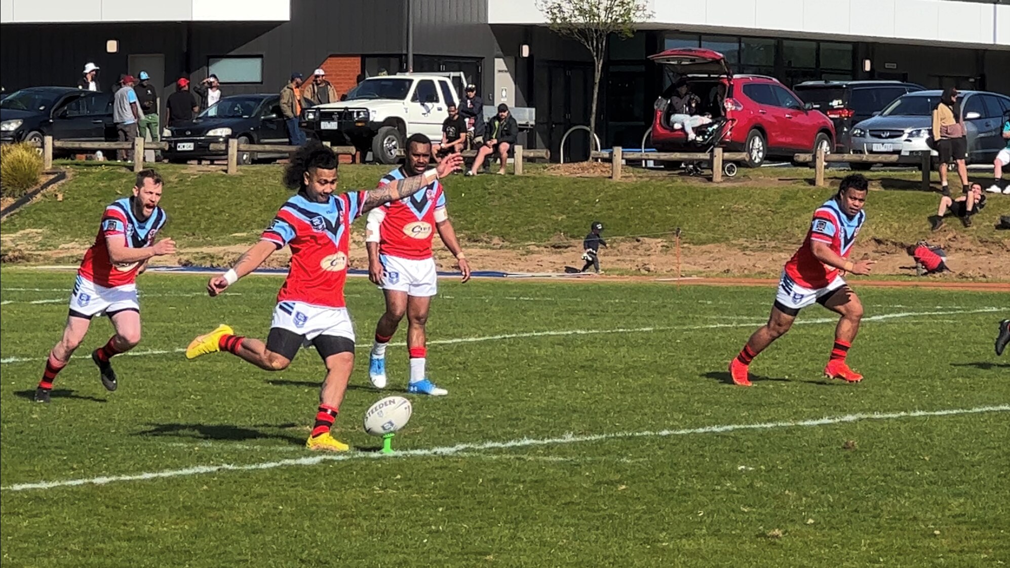 a man with slicked back long curly hair takes a kick of a rugby ball. his teammates spring behind him