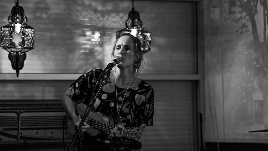 A black and white image of a woman playing the ukulele and singing into a microphone