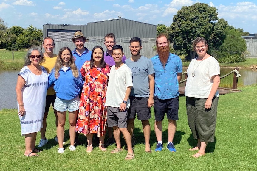 A group of smiling adults outside on a lawn on a sunny day