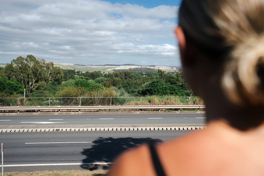 over the shoulder view of a young woman looking at a coal mine in the distance